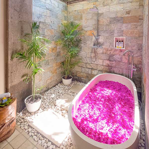 Gorgeous luxury outdoor bathroom with stone wall and rose petal bath in Bali retreat, Bliss Retreat Room, Bliss Sanctuary For Women, Canggu